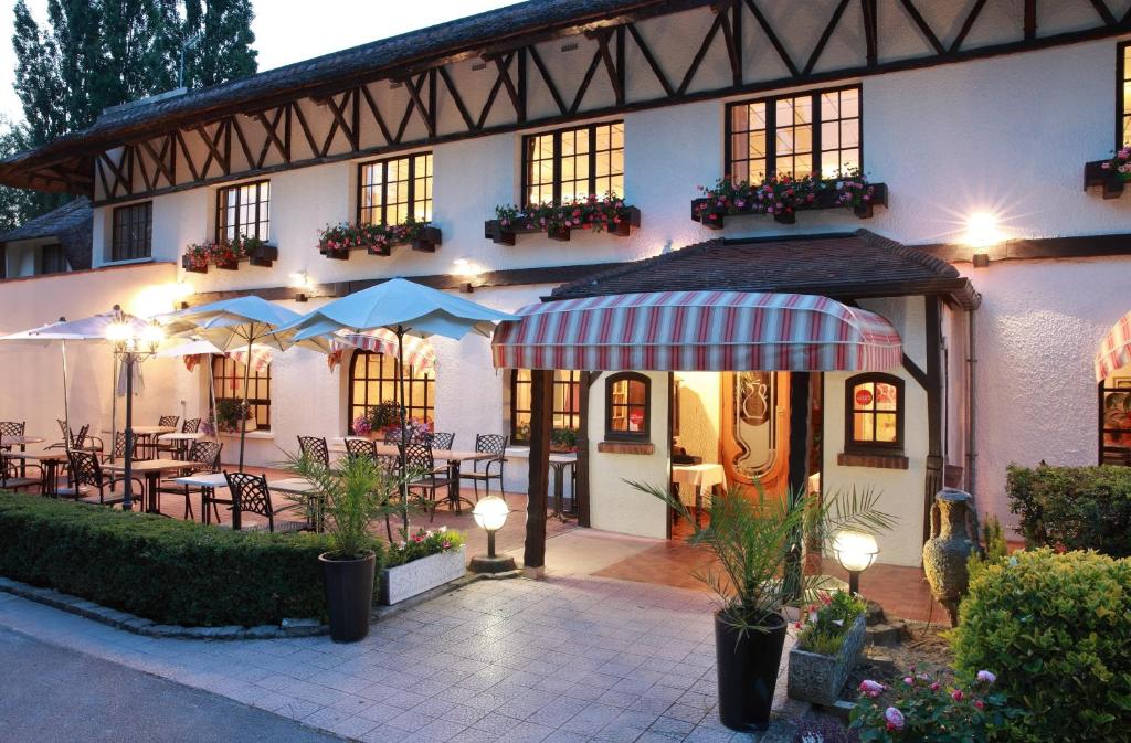 a building with tables and umbrellas in front of it at LOGIS Le Pot D'Etain in Holnon