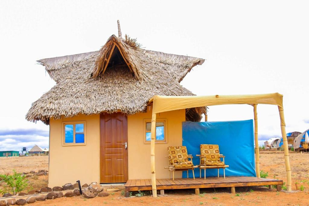 a small house with a thatched roof and two chairs at Amanya Zebra 1-Bed Wigwam in Amboseli in Amboseli
