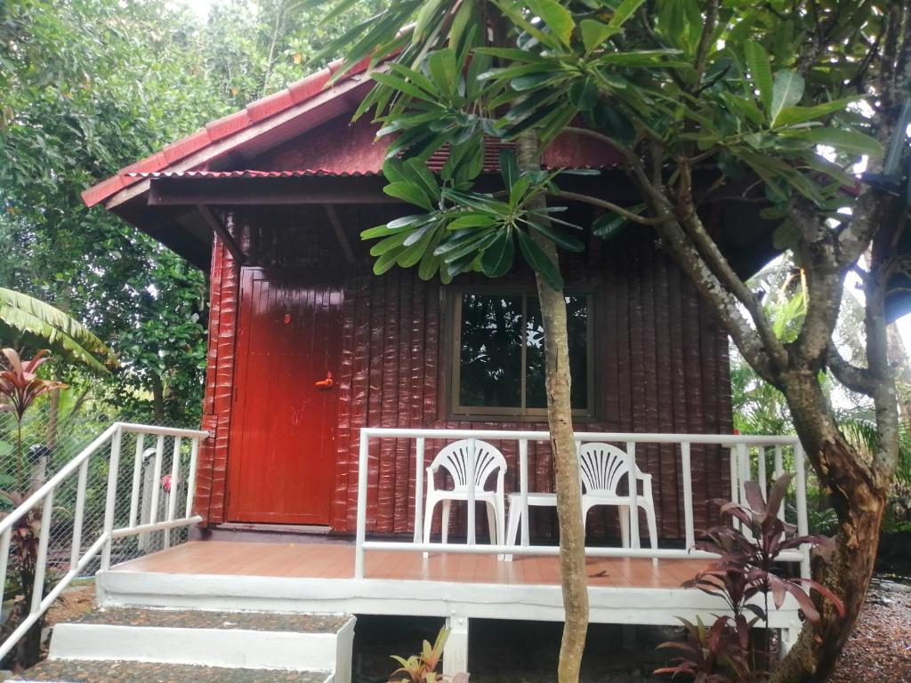 een klein rood huis met twee witte stoelen ervoor bij Thai Garden​ Resort​ Kanchanaburi​ in Kanchanaburi