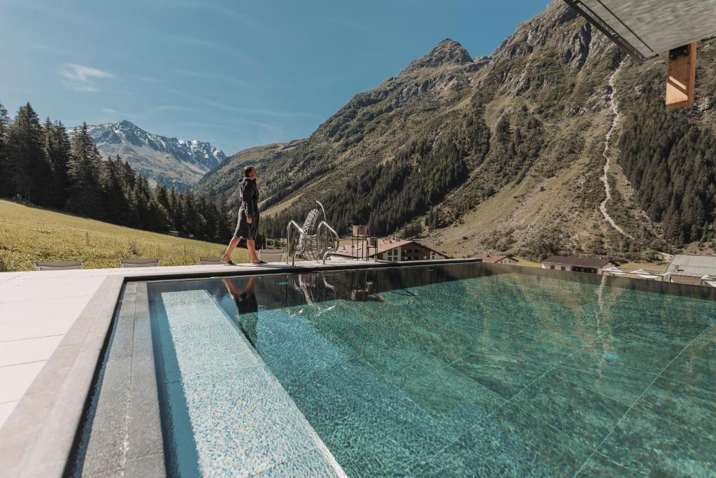 a man walking by a swimming pool with a mountain at Alpine Resort Sportalm in Sankt Leonhard im Pitztal