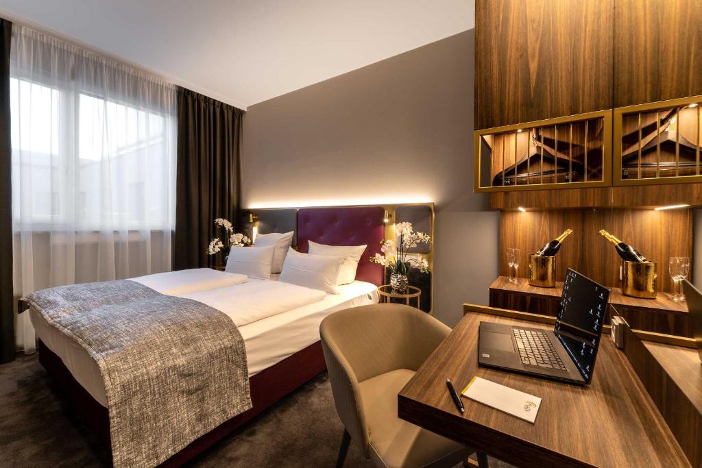 a hotel room with a bed and a desk with a laptop at PLAZA Premium München in Munich