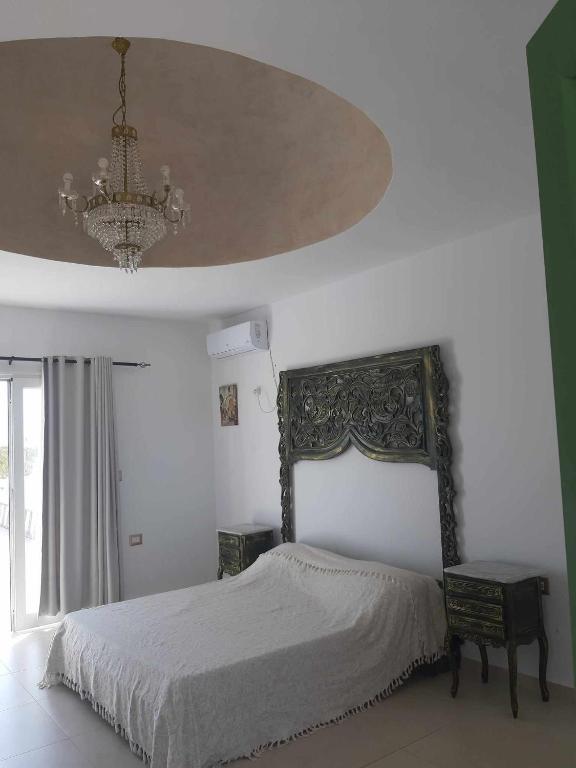 - une chambre avec un lit et un lustre dans l'établissement Magnifique appartement djerbien, à El Guecheïne