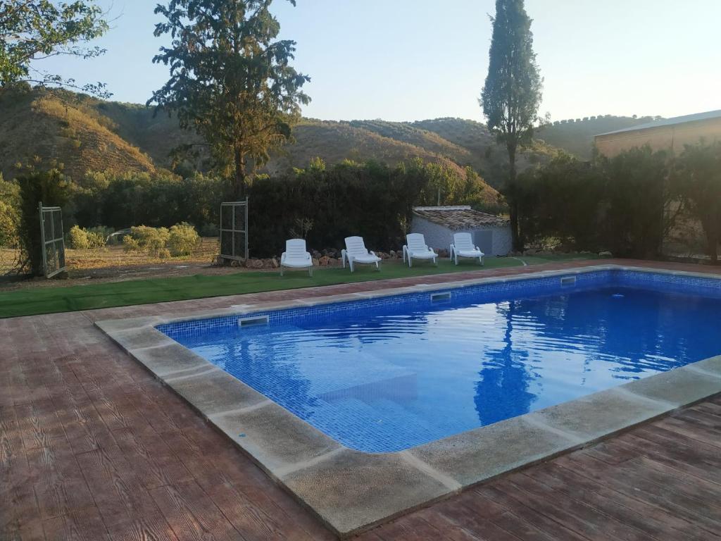 uma piscina num quintal com duas cadeiras brancas em Casa La Masía de Córdoba em Almedinilla
