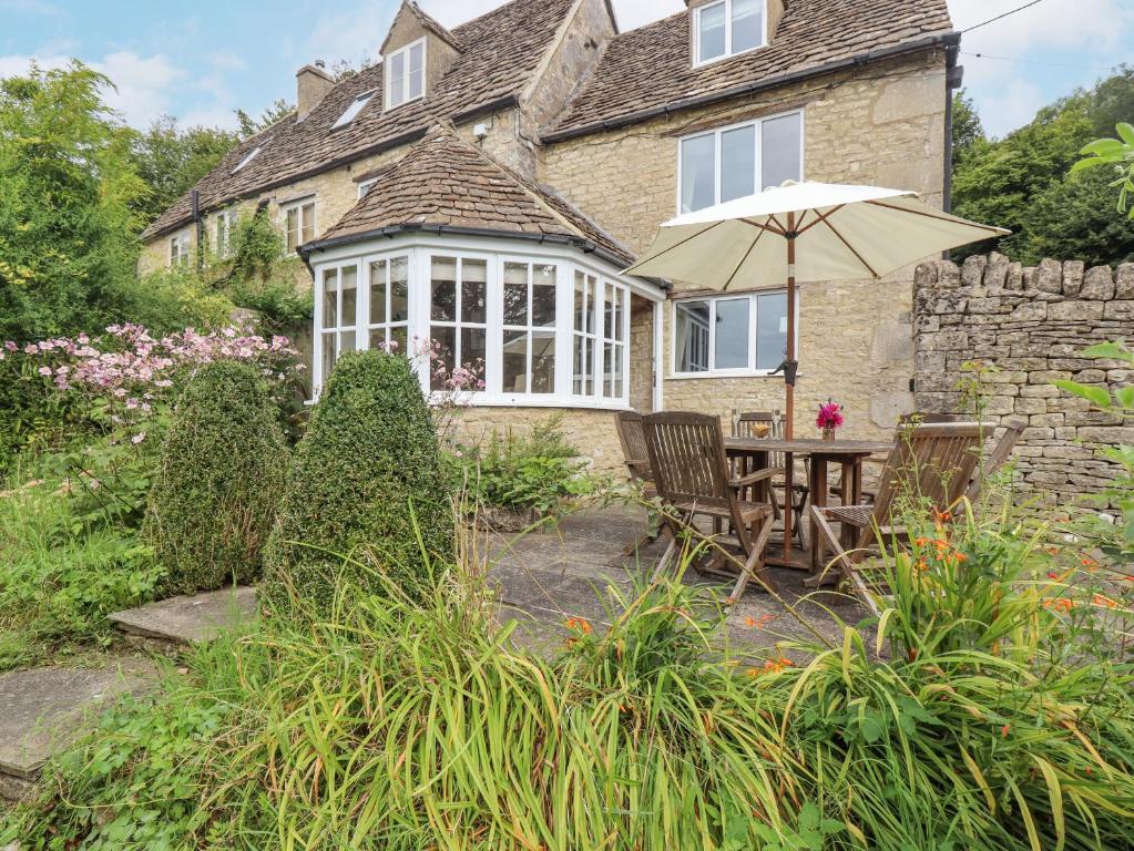 a house with an umbrella and a table and chairs at Grange Cottage in Woodchester