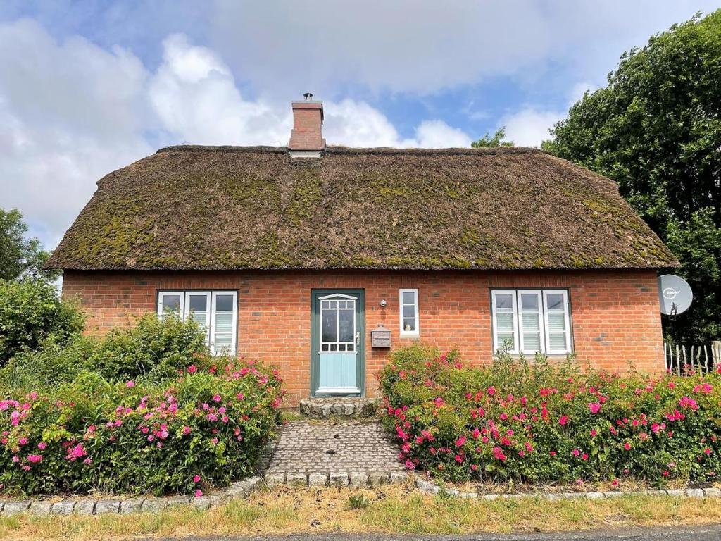 een stenen huis met een rieten dak met bloemen bij Das Puppenhaus, Reetdach, Sauna, Kamin, eingezäunt, Badewanne, Haustiere willkommen in Emmelsbüll-Horsbüll