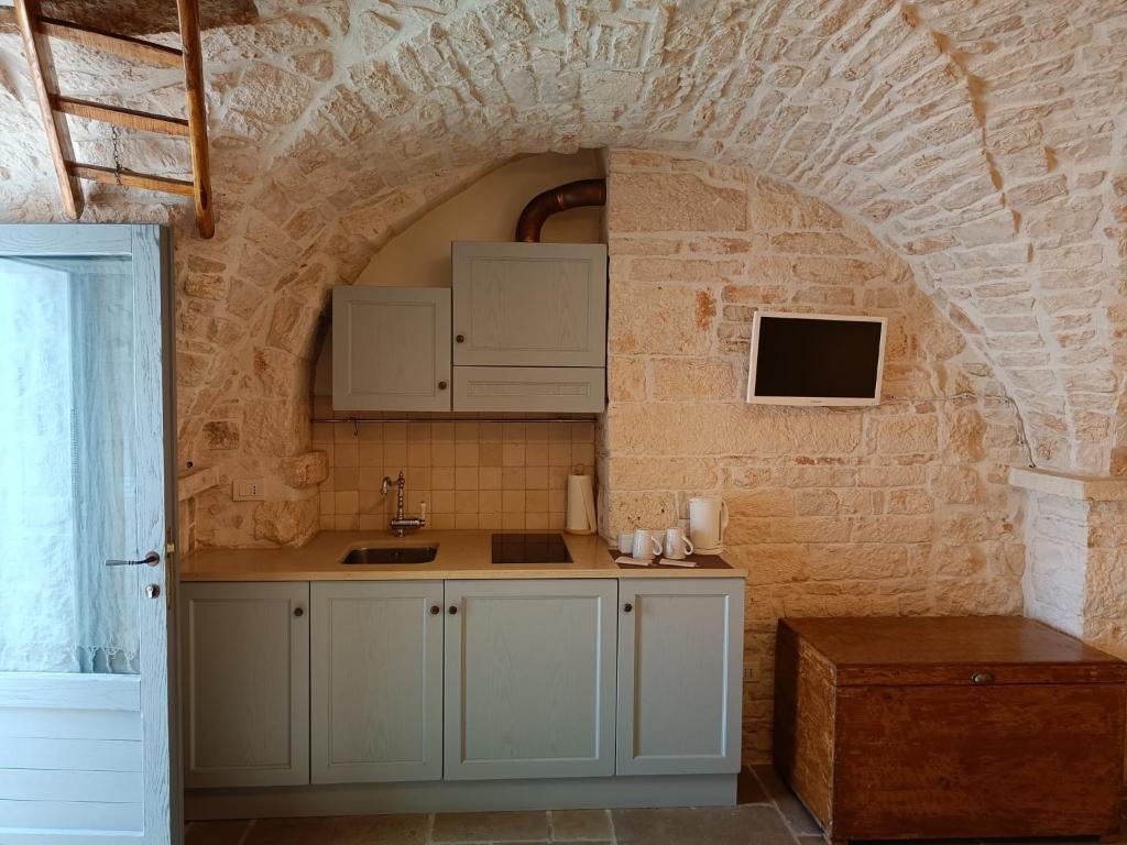 une cuisine avec des placards blancs et un mur en briques dans l'établissement Trulli D'Angiò, à Alberobello