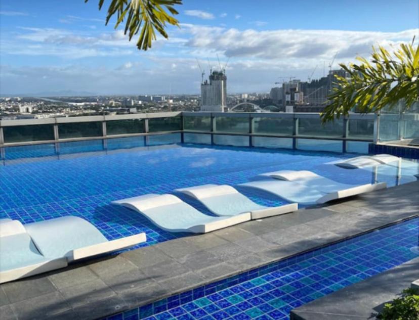 Classy 2BR Suite at Eastwood City with Pool and City Skyline View في مانيلا: مسبح مع كراسي جلوس فوق المبنى