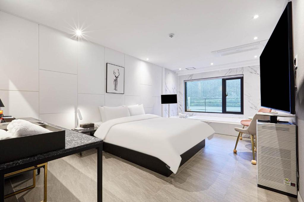 a white bedroom with a large bed and a desk at The Amber Hotel in Yangpyeong