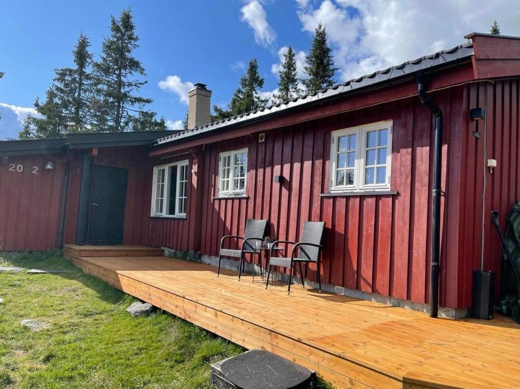 ein rotes Haus mit zwei Stühlen auf einer Holzterrasse in der Unterkunft Buhaug - cabin at Sjusjøen in Ringsaker