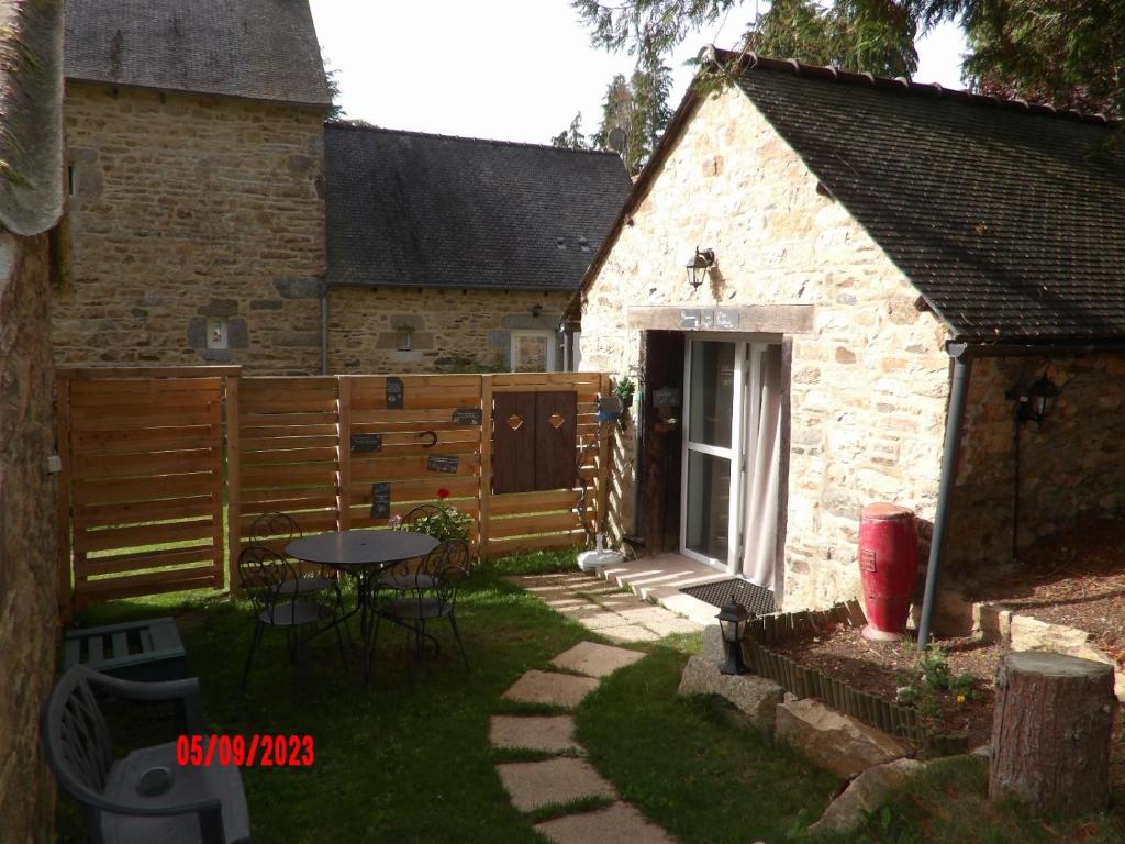 een achtertuin van een stenen gebouw met een tafel en een hek bij Le cheval d’en fer in Bégard