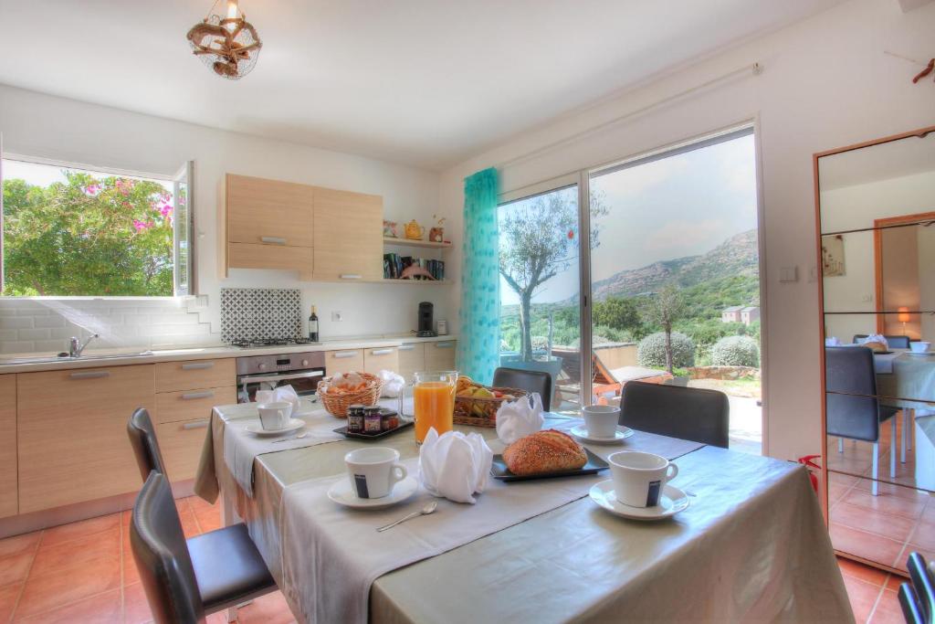 a dining room with a table and a kitchen with large windows at Les Oliviers CENTURI-PORT in Centuri