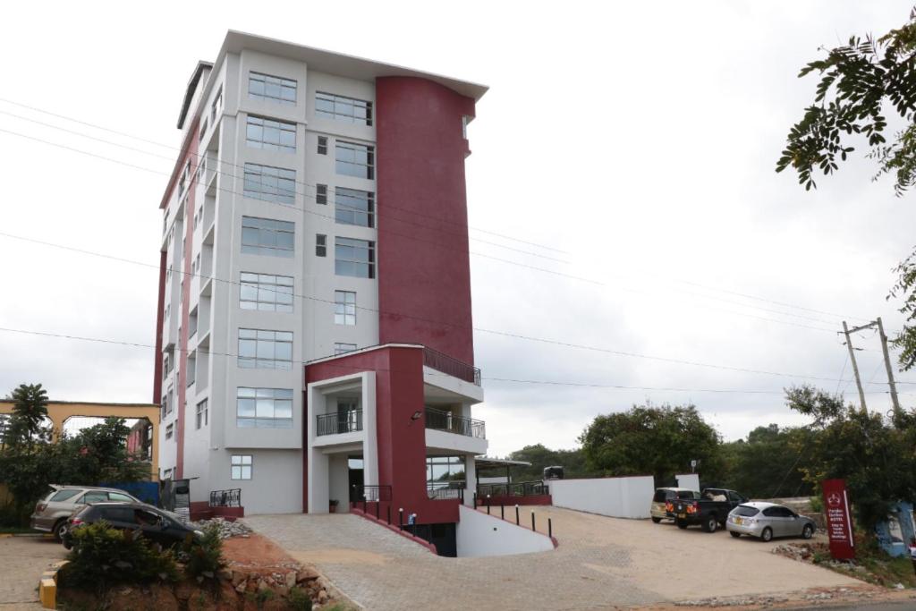 un edificio rojo alto con coches estacionados en un estacionamiento en Paraiso Gardens Hotel, en Wote