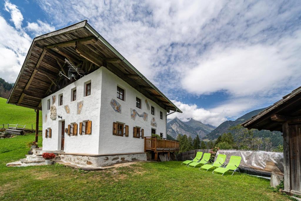 a white building with green chairs in a field at Ferienhaus Engele in San Martino