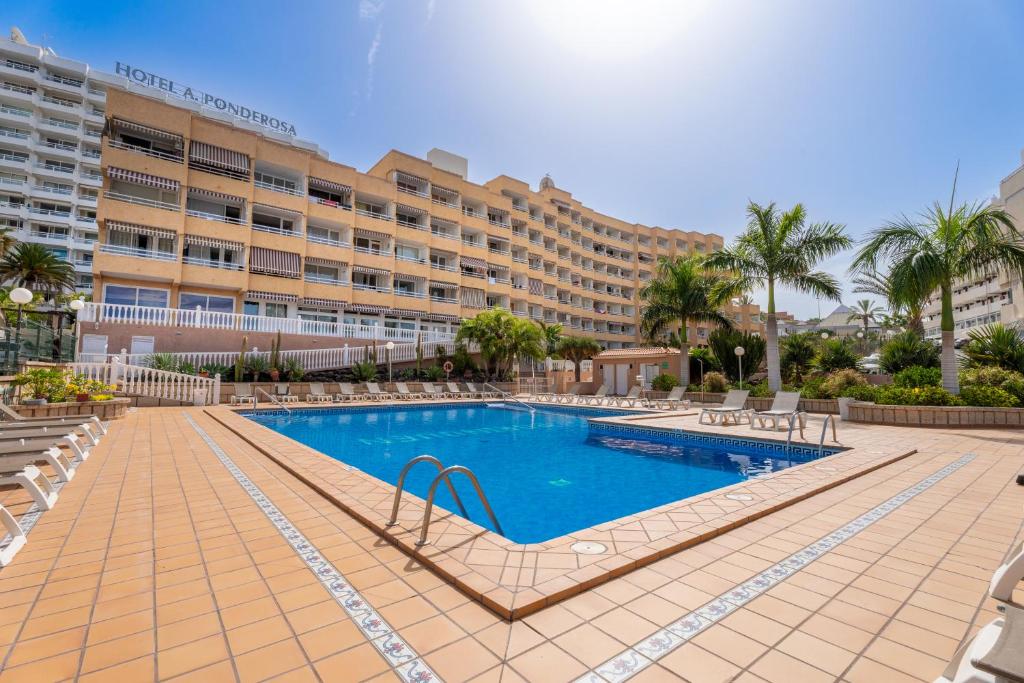 uma piscina de resort com um hotel ao fundo em Apartamentos Borinquen em Playa de las Americas