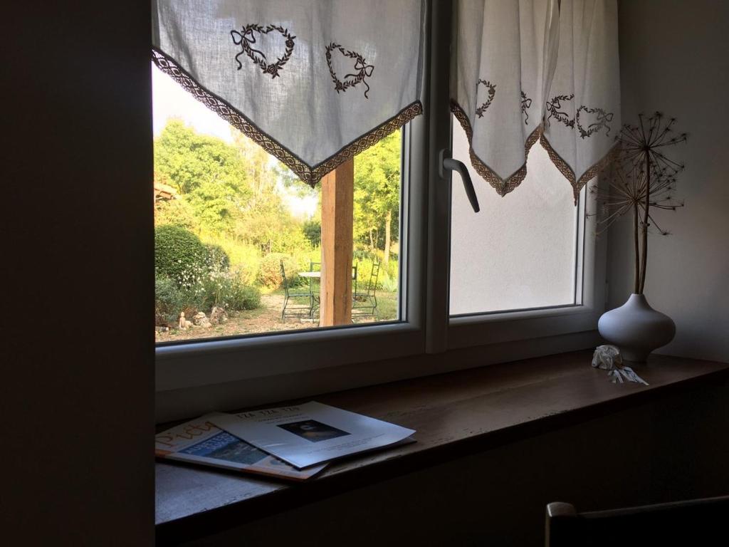 a window with curtains and a book on a counter at Maison d hôtes Les Chantours dans réserve naturelle 15 hectares in Saint-Antoine-Cumond