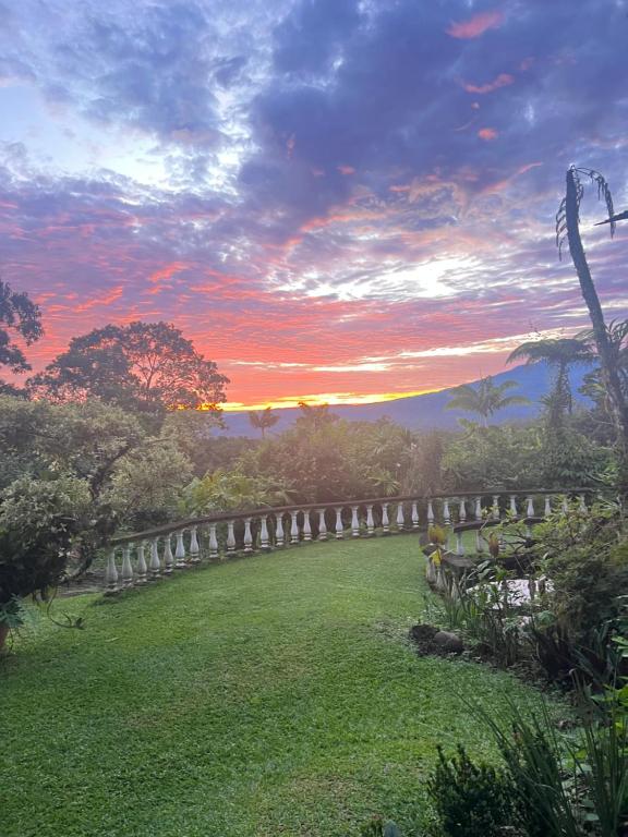 een zonsondergang boven een grasveld met een hek bij Botanica Gardens and Eco Lodge in San Gerardo
