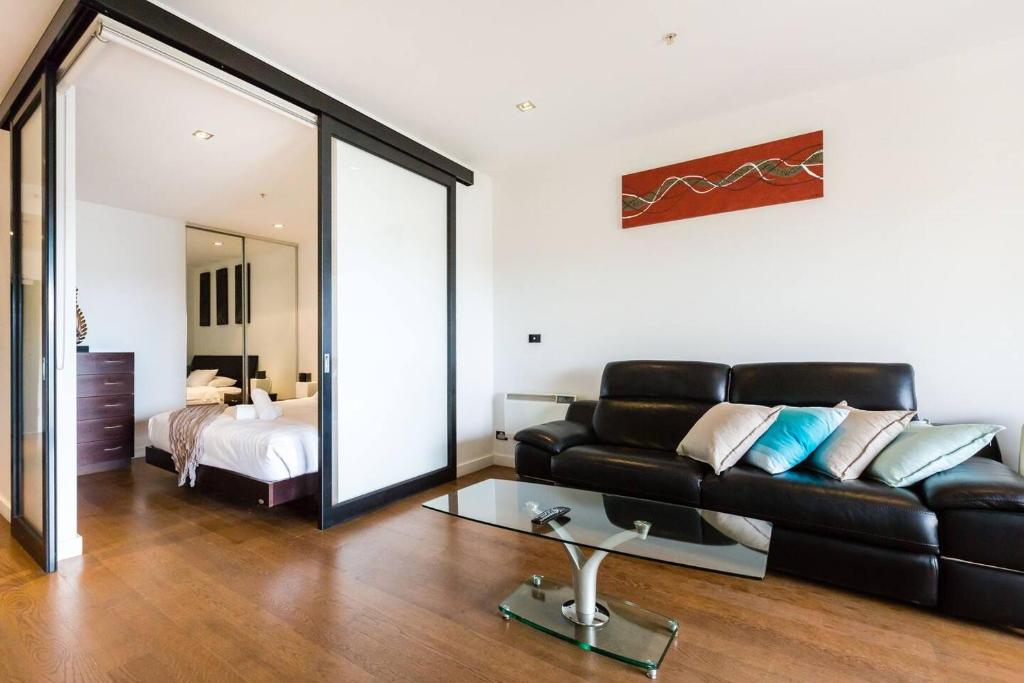 sala de estar con sofá de cuero negro y cama en Southside St Kilda Seclusion with Balcony and Parking, en Melbourne