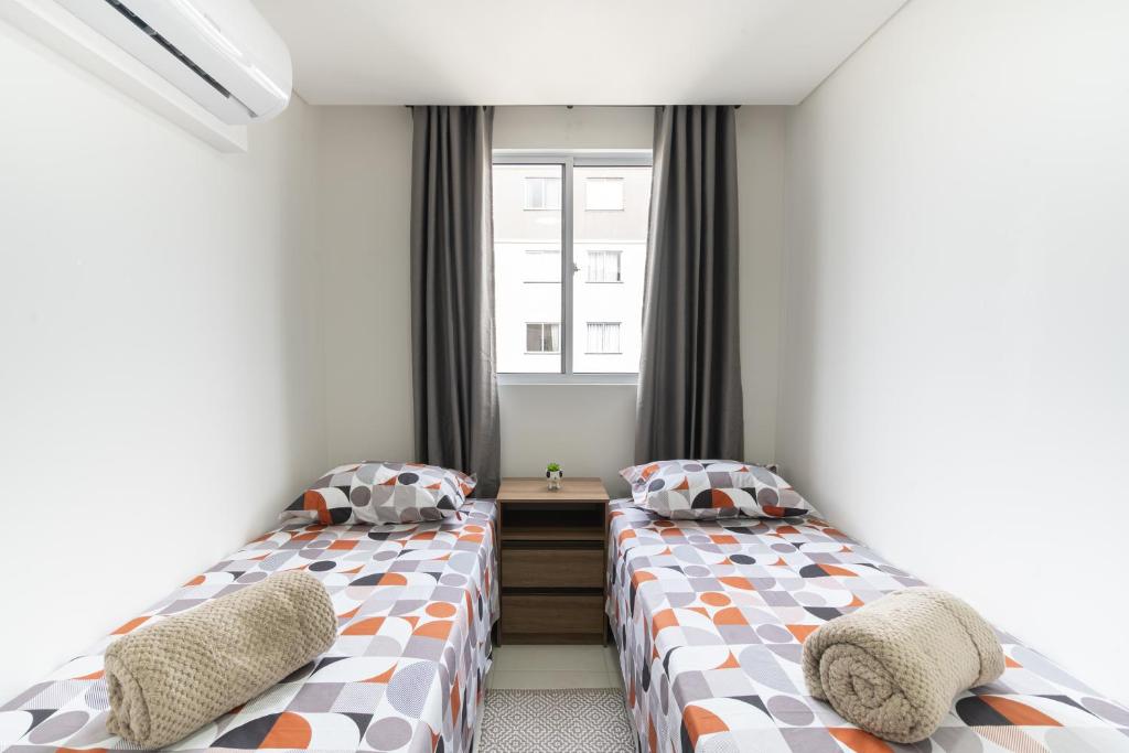two beds in a small room with a window at Apartamento com VISTA MAR, Ar-condicionado, Wi-Fi Condomínio com PISCINA, quadra de esportes Playground infantil a 15 minutos do Beto Carreiro in Piçarras