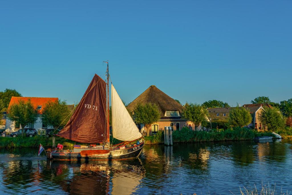 un velero en el agua junto a una casa en Appartement Avondzon in romantische stolpboerderij, en Warmenhuizen