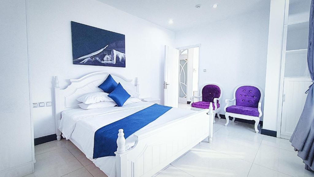 a bedroom with a white bed and two purple chairs at Queen Central Apartment Hotel in Ho Chi Minh City