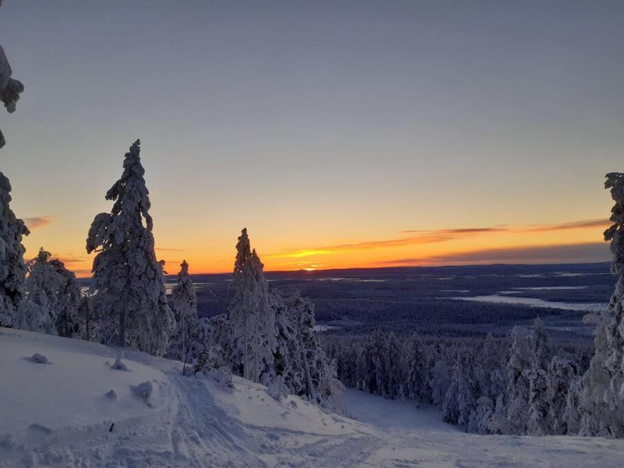 a snow covered hill with trees and a sunset at Levi Holiday home Poroileville in Kittilä