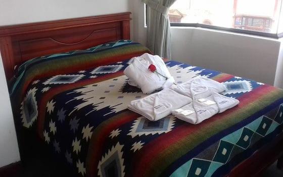 a bed with a colorful comforter with towels on it at Coraza Hotel in Otavalo