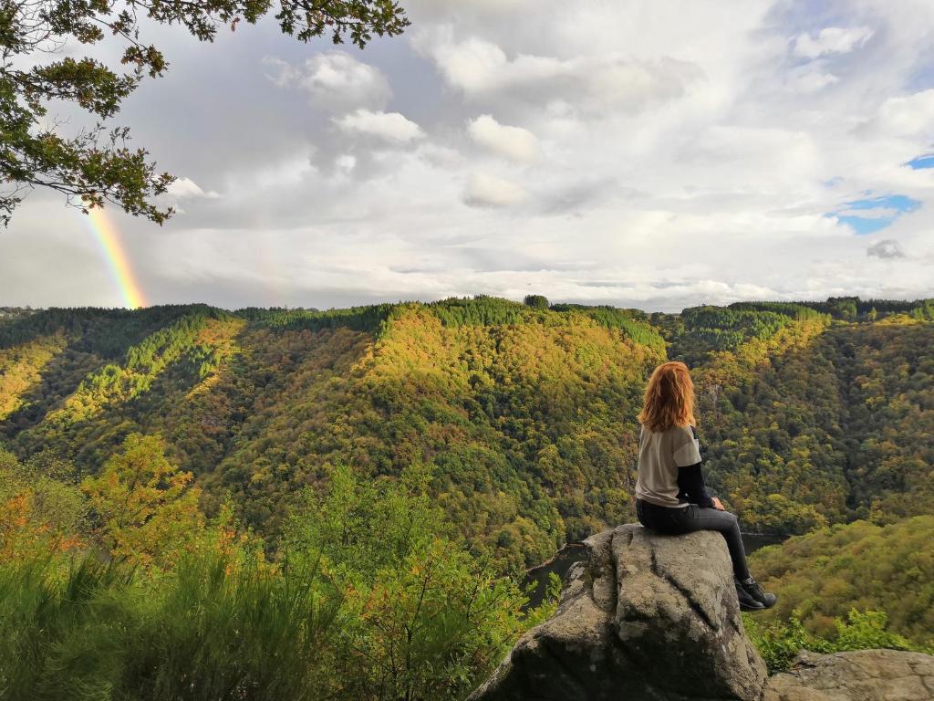 a woman sitting on a rock watching a rainbow at Gîte du Busatier in Marcillac-la-Croisille