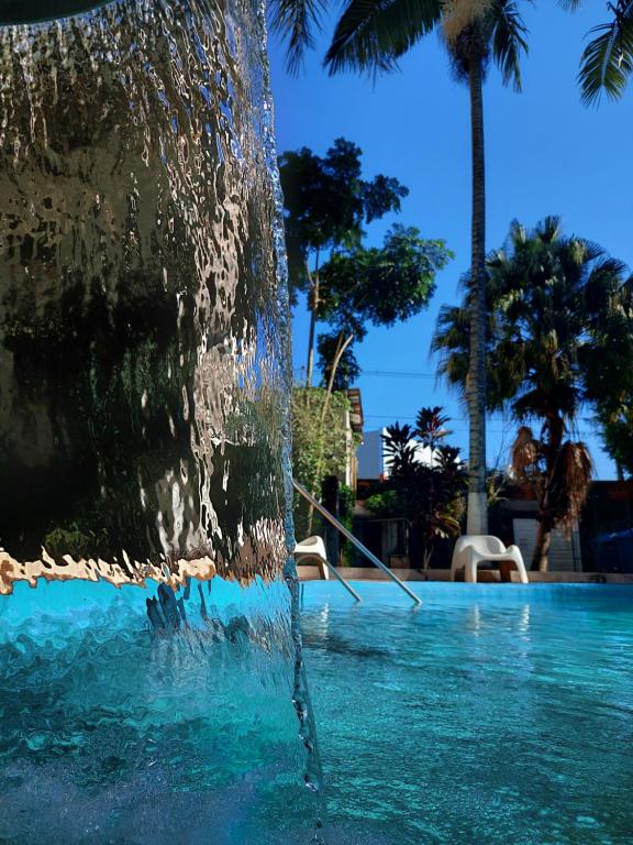 a water fountain in a swimming pool with palm trees at Hotel Castelo Branco in Foz do Iguaçu