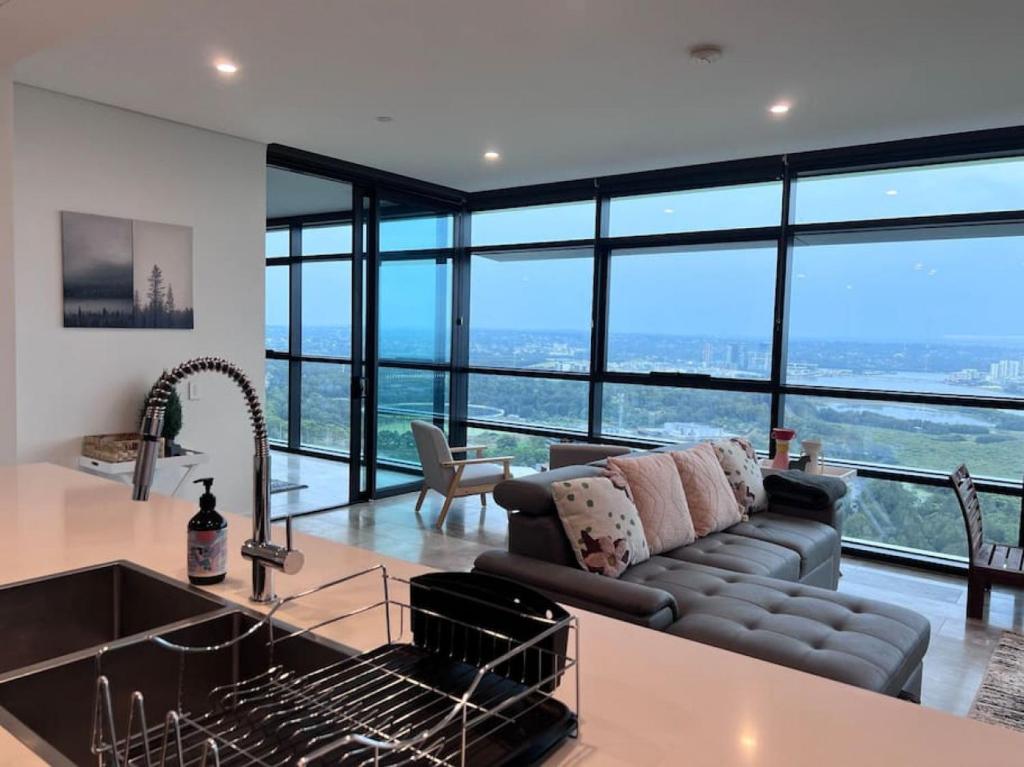 een keuken en een woonkamer met een bank en grote ramen bij High Level Fabulous View 4Beds APT in Olympic Park in Sydney