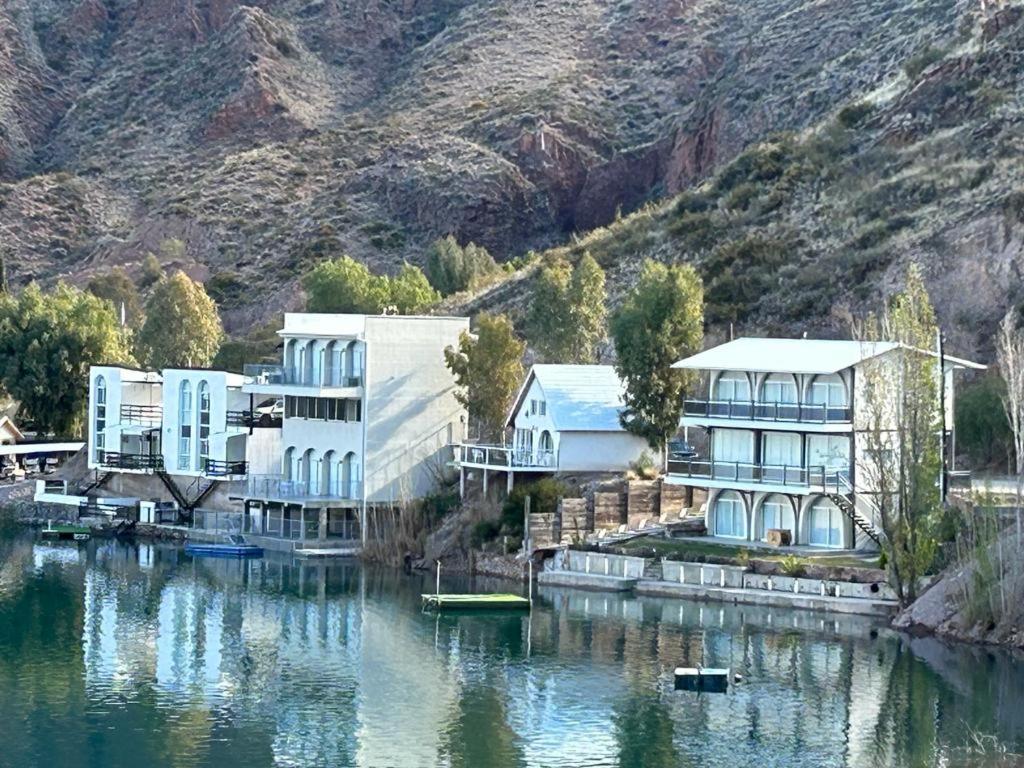 a building on the water next to a mountain at Casa en Los Reyunos, Ubicación perfecta Frente al lago in San Rafael