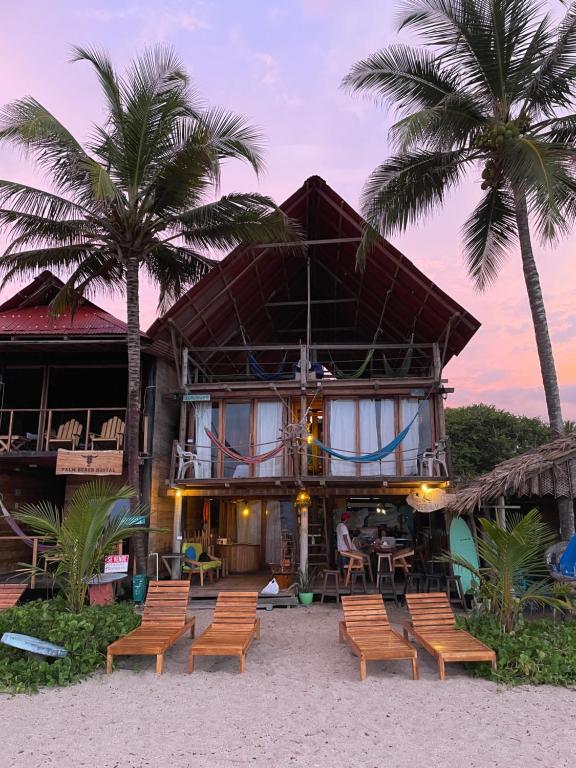 una casa sulla spiaggia con sedie e palme di Hostal velero relax a Santa Marta