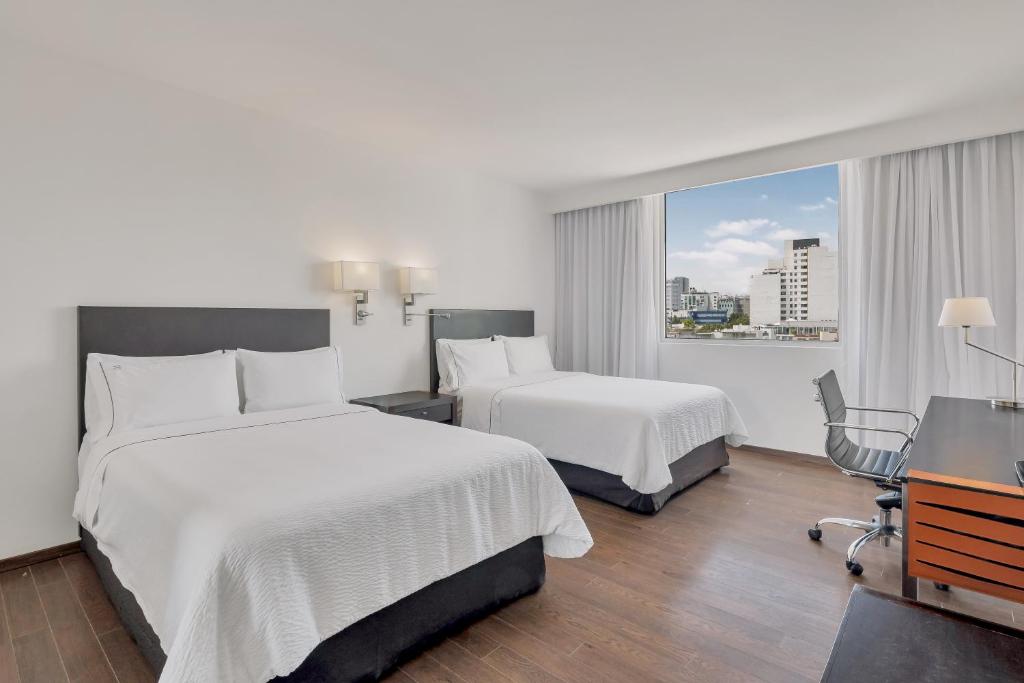 A twin room with two beds, work desk and a broad urban window view.