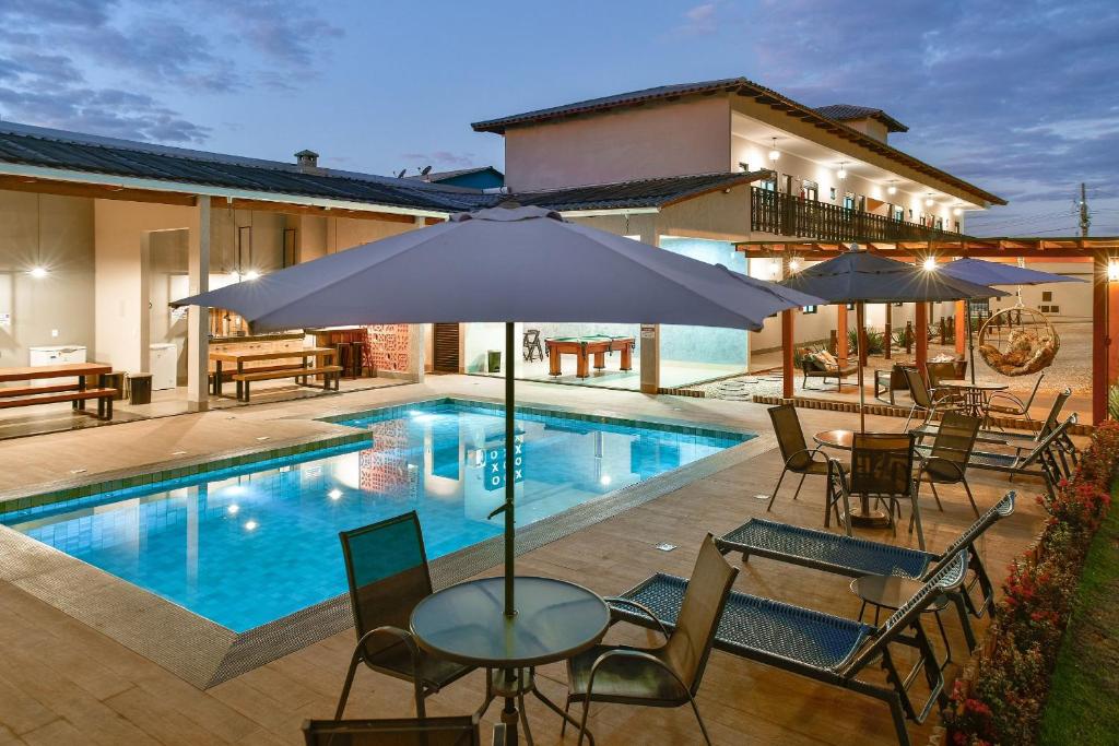 a swimming pool with tables and chairs and an umbrella at Flats Charme do Cerrado in Pirenópolis