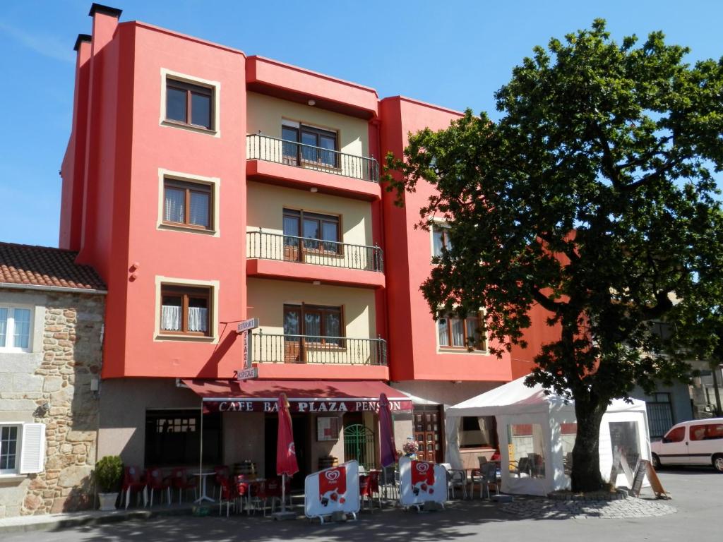 un edificio rojo con un árbol delante de él en Pensión Plaza, en Quintáns