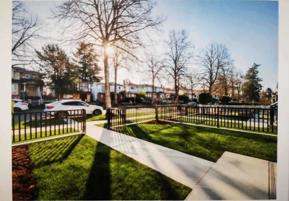 a fence in a park with a sidewalk and grass at Lucy's Place - Two Bedroom Suite in Vancouver