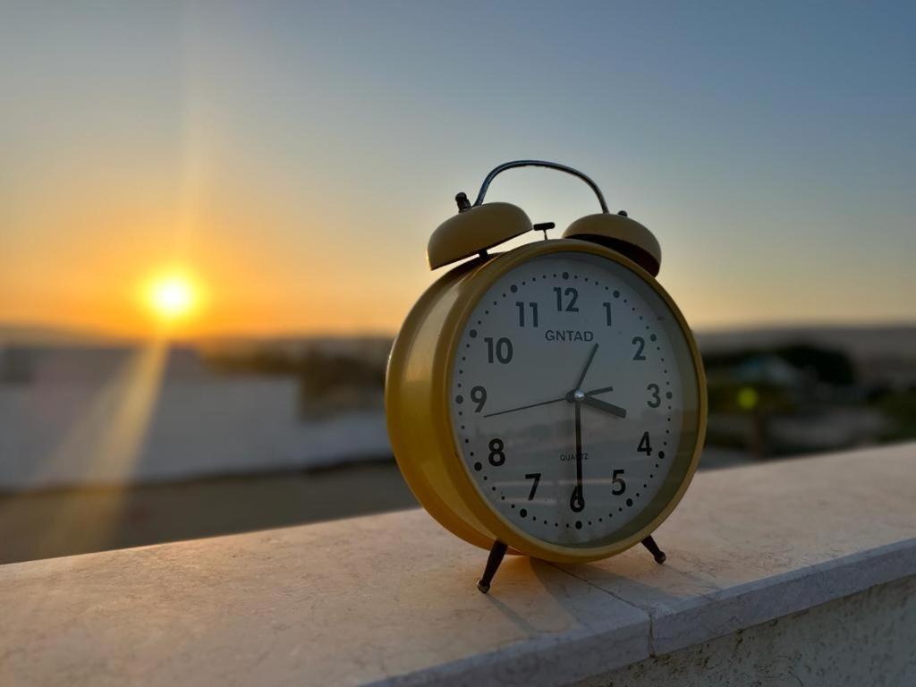 un reloj sentado en una cornisa con la puesta de sol en el fondo en רגע של מדבר en Yeruham