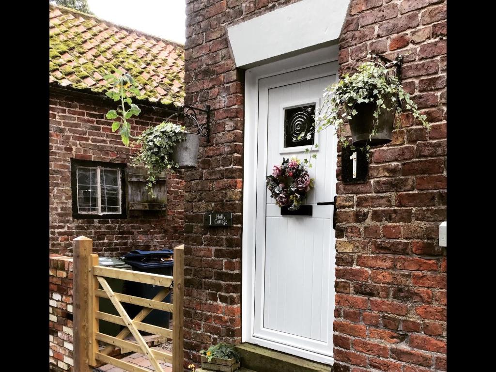 Una porta bianca su una casa di mattoni con dei fiori sopra di Holly cottage Wold Newton, near Yorkshire coast a Wold Newton