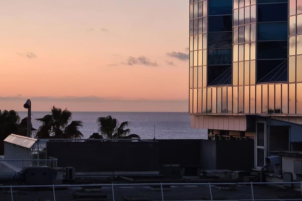 - une vue sur un bâtiment et l'océan au coucher du soleil dans l'établissement Face mer et plages appartement avec terrasse., à Nice