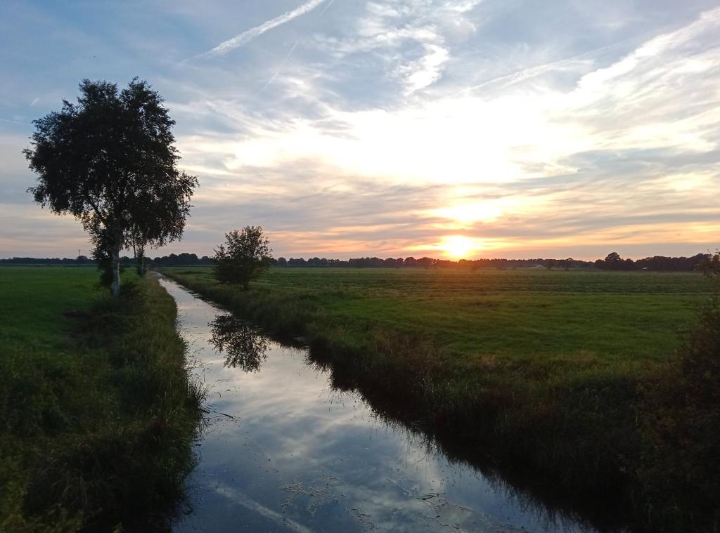 un río en un campo con la puesta de sol en el fondo en Salthuus Ostfriesland en Friedeburg