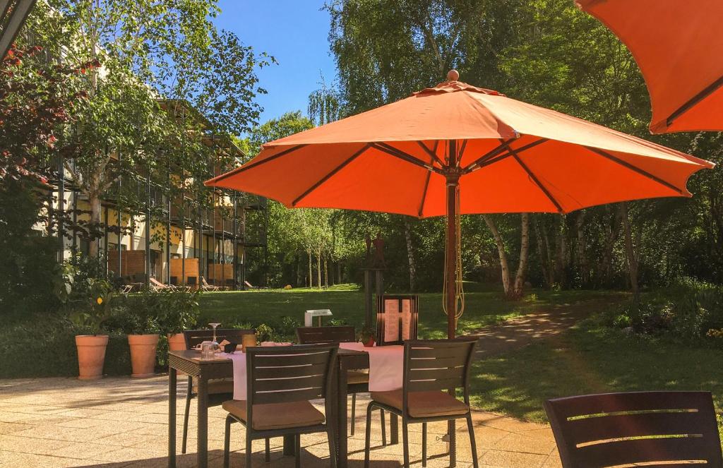 a table with an orange umbrella and chairs under it at Heide Spa Hotel &amp; Resort in Bad Düben