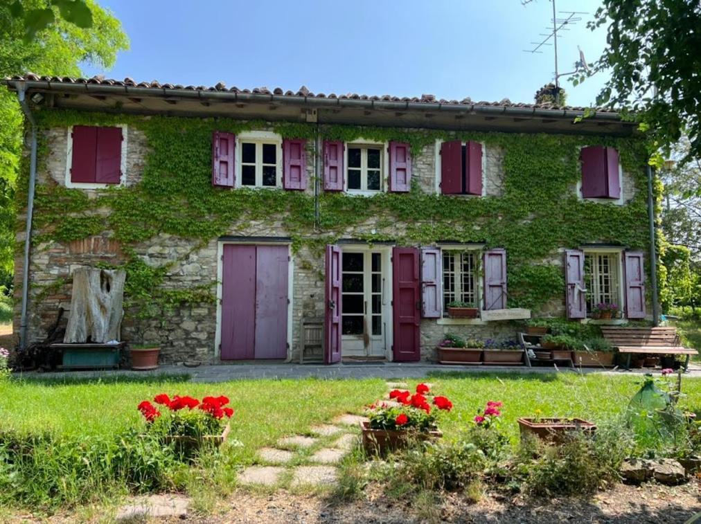 una vecchia casa in pietra con porte rosse e fiori rossi di B&B Casa dei Cuori - Natura, Silenzio, relax a 550 m di quota a Langhirano