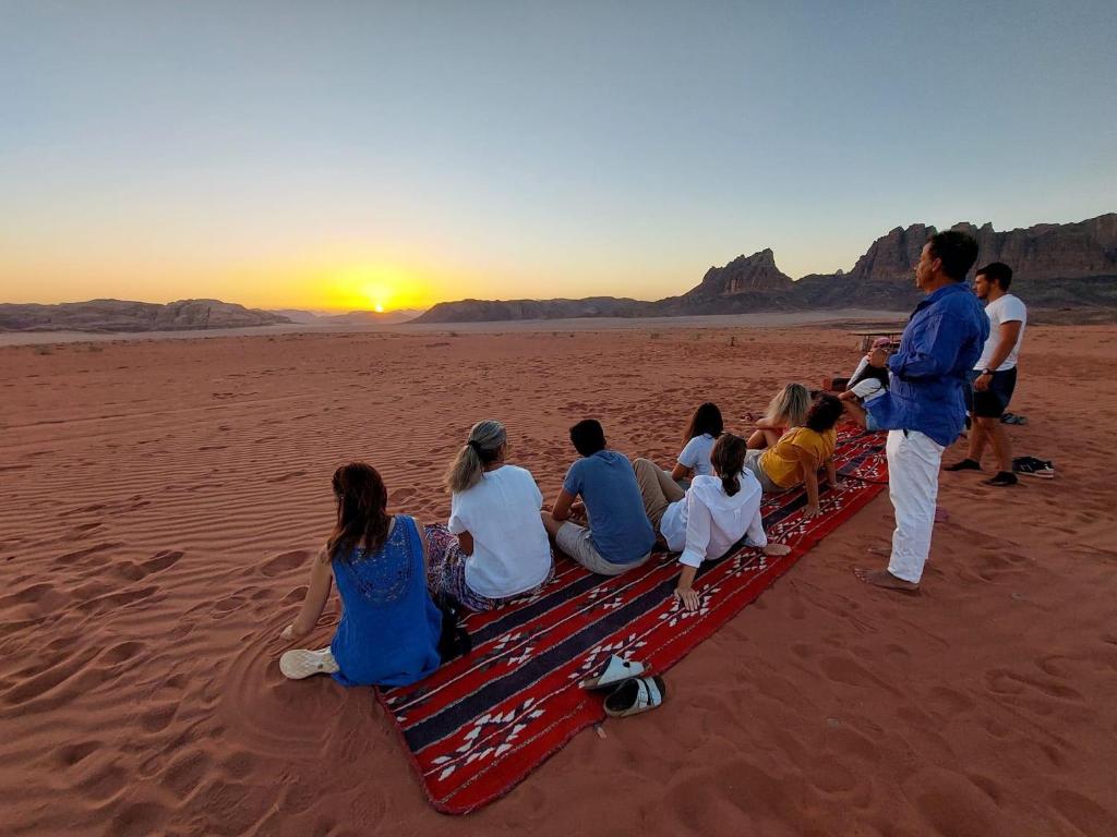 a group of people sitting on a beach watching the sunset at bedouin future camp in Wadi Rum