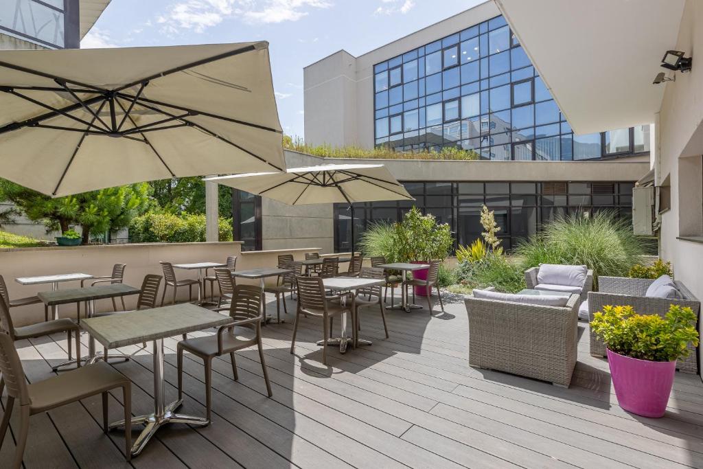 un patio al aire libre con mesas, sillas y sombrillas en Les Loges du Park en Aix-les-Bains