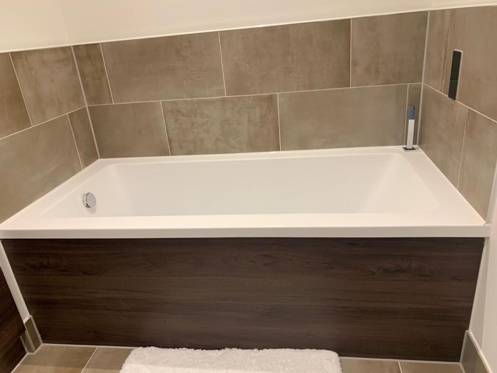 a white bath tub in a bathroom with a tile wall at Ackroyd House, Edinburgh Way in Harlow