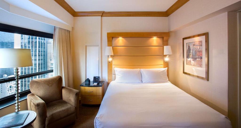 a hotel room with a bed and a chair and a window at New York Hilton Midtown in New York