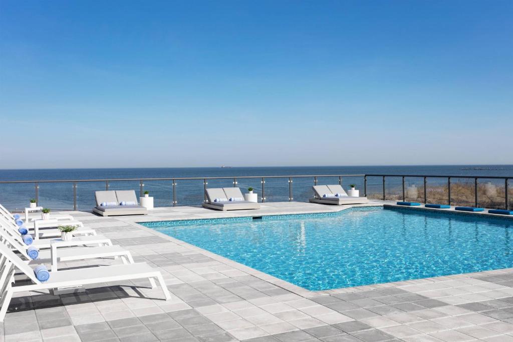 a swimming pool with lounge chairs and the ocean at Delta Hotels by Marriott Virginia Beach Waterfront in Virginia Beach