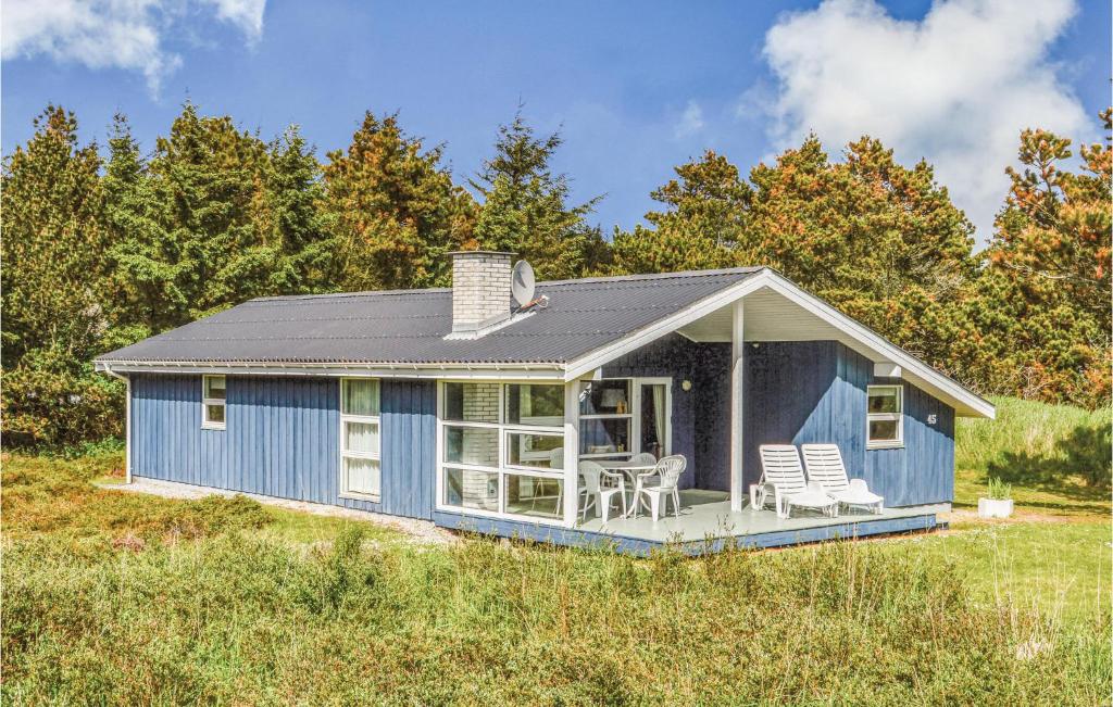 a blue tiny house with a deck in a field at Amazing Home In Ringkbing With 3 Bedrooms, Sauna And Wifi in Klegod