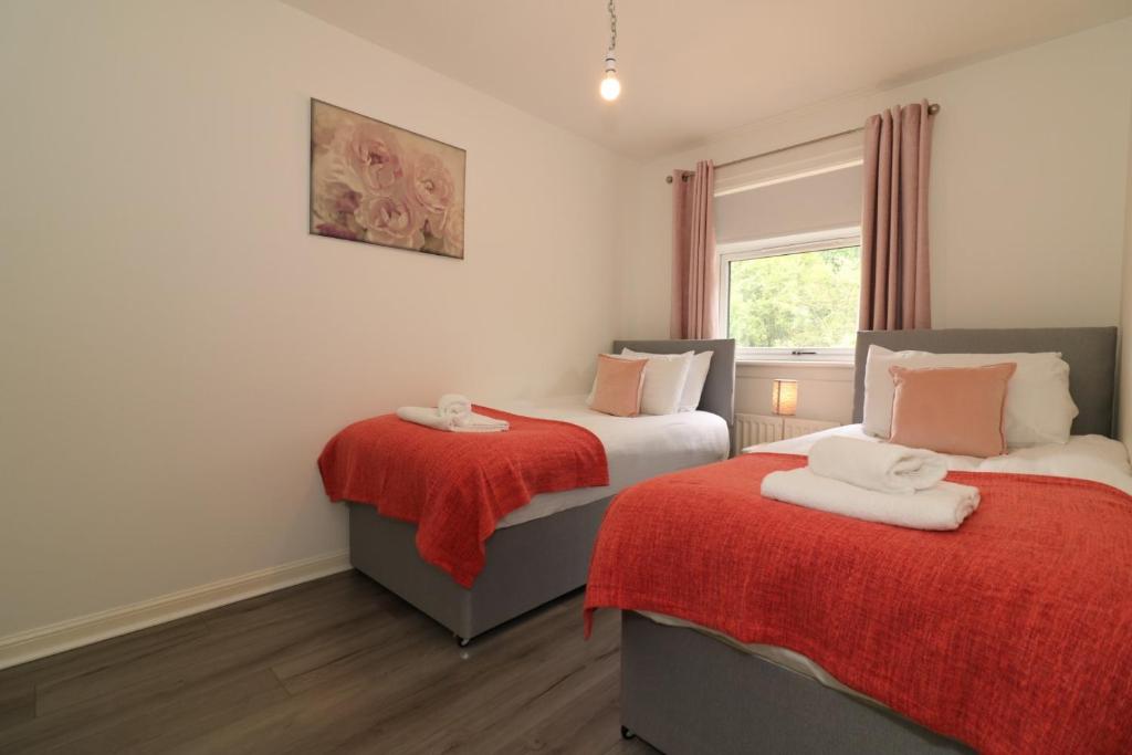 a bedroom with two beds with red sheets and a window at Signature - Culzean House in Newarthill