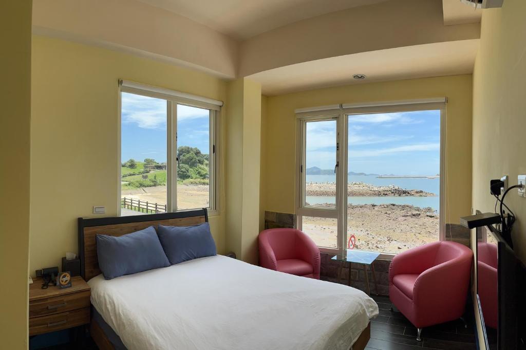 南竿鄉的住宿－馬祖藍灣景觀餐廳民宿南館，一间卧室配有一张床和两把椅子,还有一个海滩