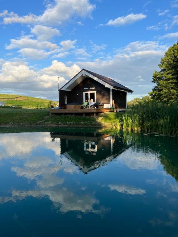a house with a reflection in the water at Milkės Karibai - poilsio namelis su sauna ir kubilu 